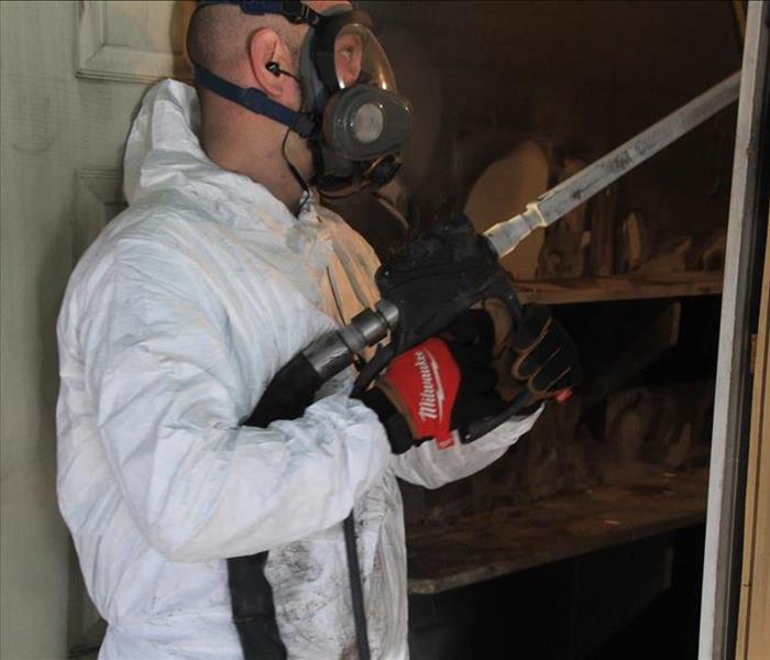 Walls with soot on them with a SERVPRO worker holding a machine to clean the walls