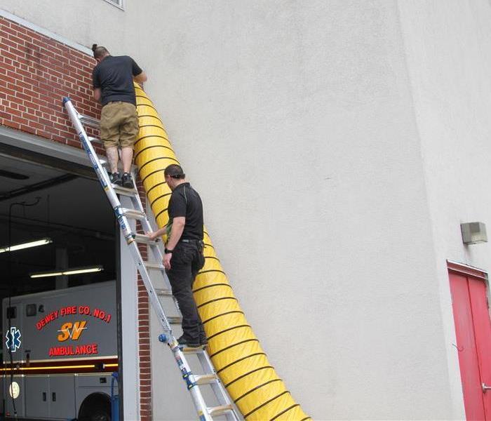 two SERVPRO workers on a ladder